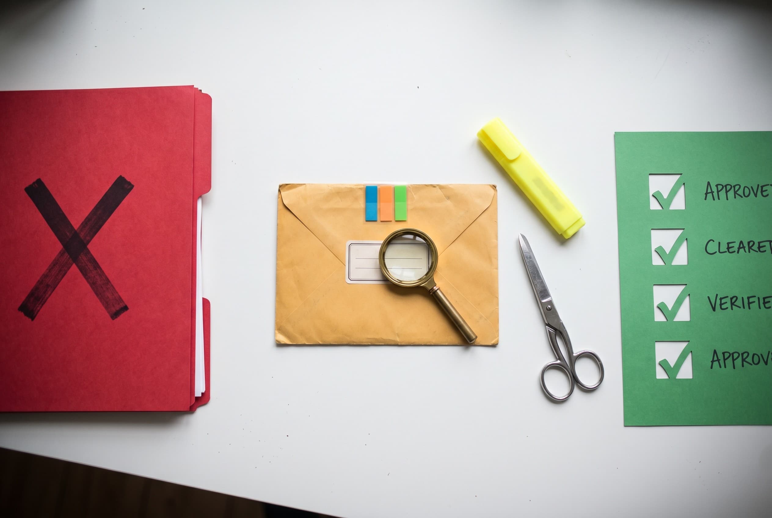 Top-down flat-lay photo on a clean white desk: on the left a red folder stamped with a large X shape representing a denial, i