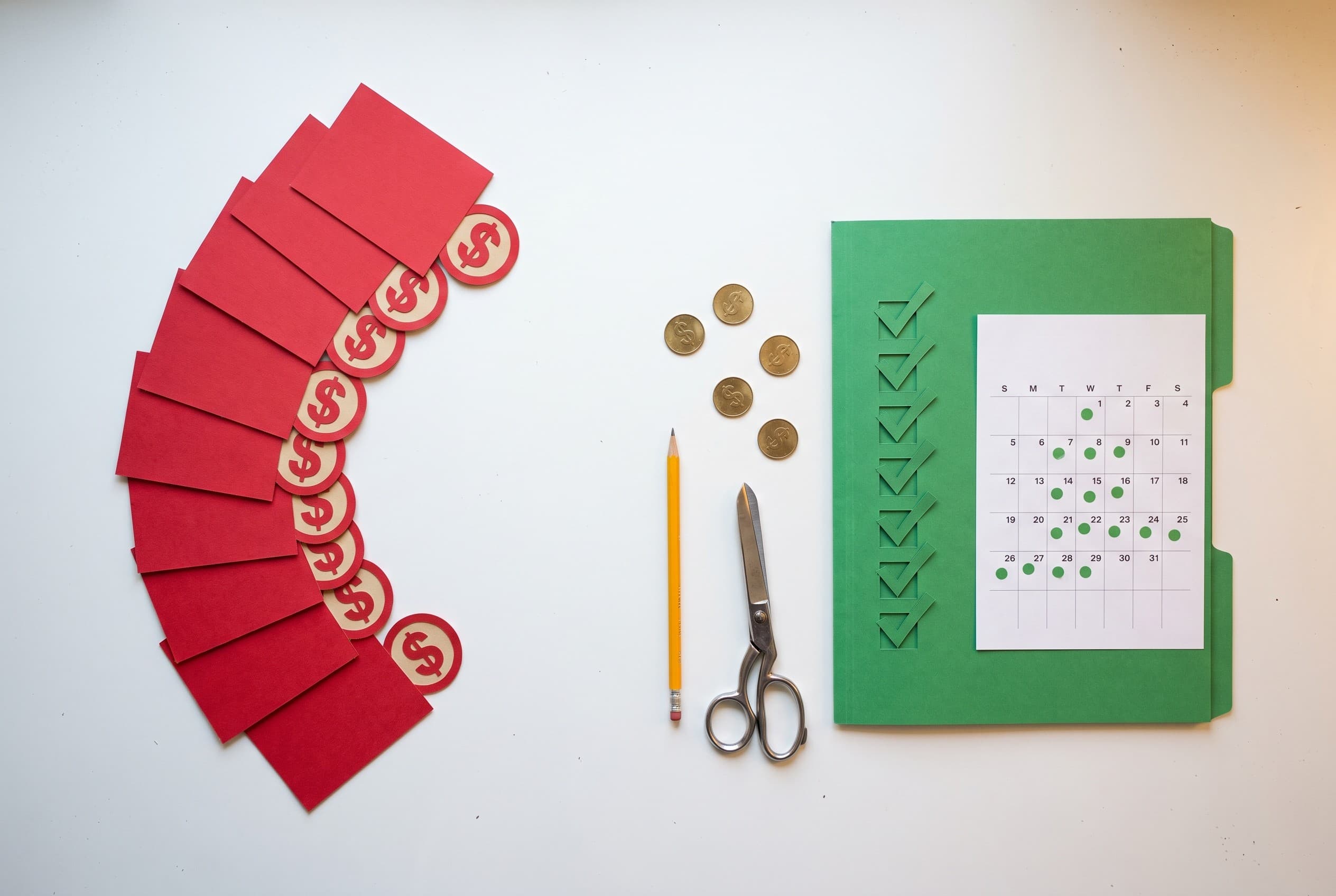 Top-down flat-lay on a clean white desk showing two paths of paper cutouts. On the left, a small stack of red paper cards fan