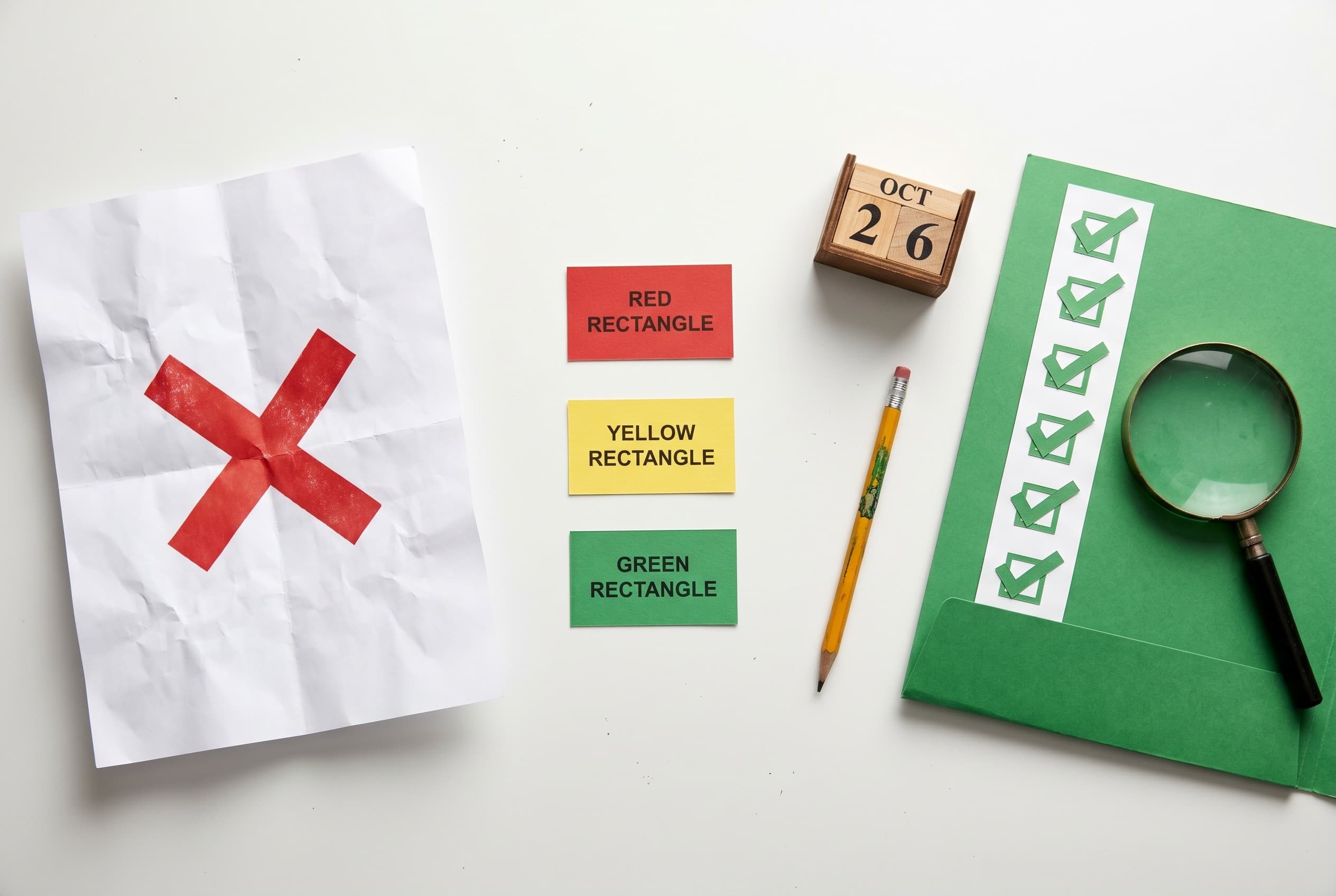 Top-down flat-lay photo of a clean white desk. On the left, a crumpled white letter with a bold red stamped X shape. In the c