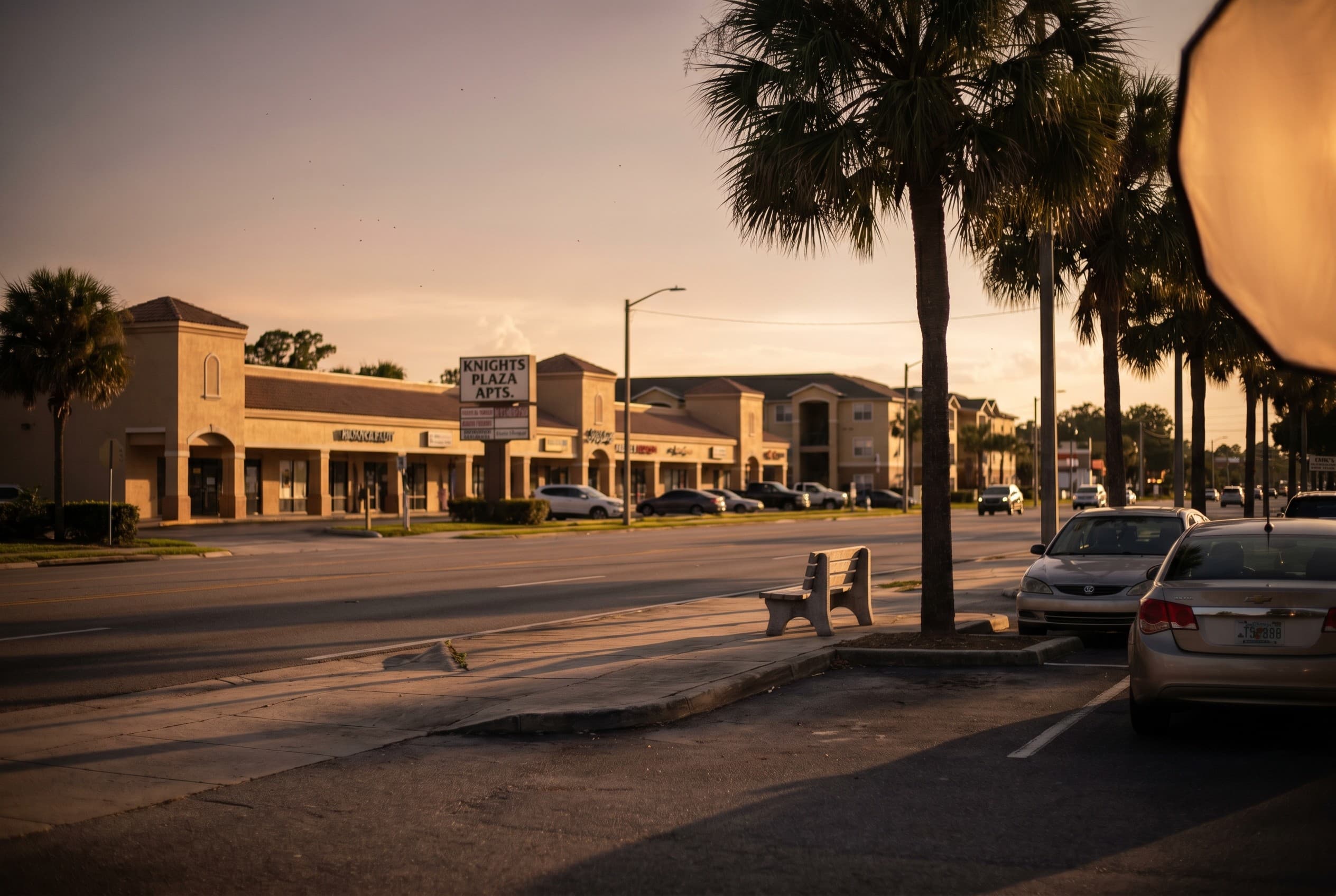 A quiet stretch of University Boulevard near the UCF area in Orlando at golden hour, shot from a parking lot looking across a