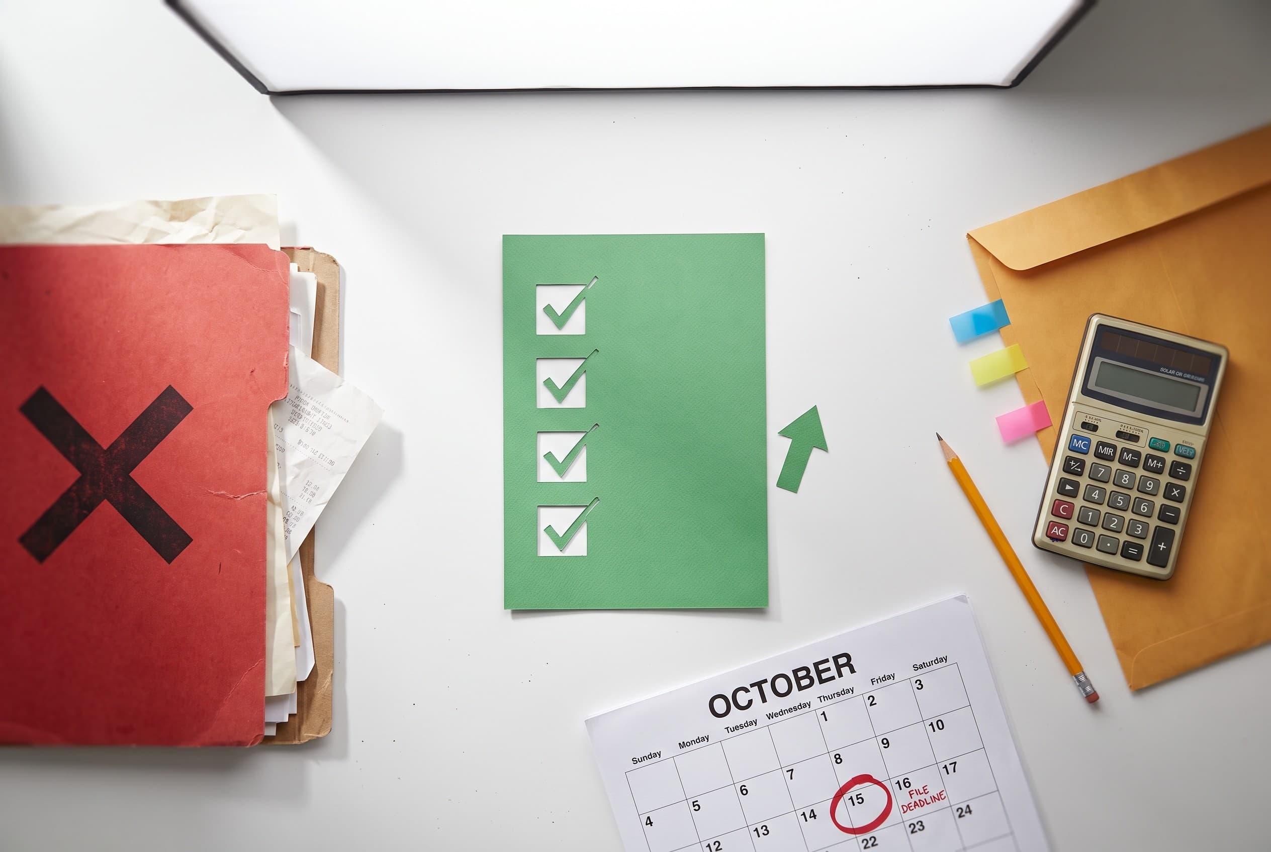 Top-down flat-lay photo on a clean white desk showing a self-employment credit story. On the left, a red folder stamped with