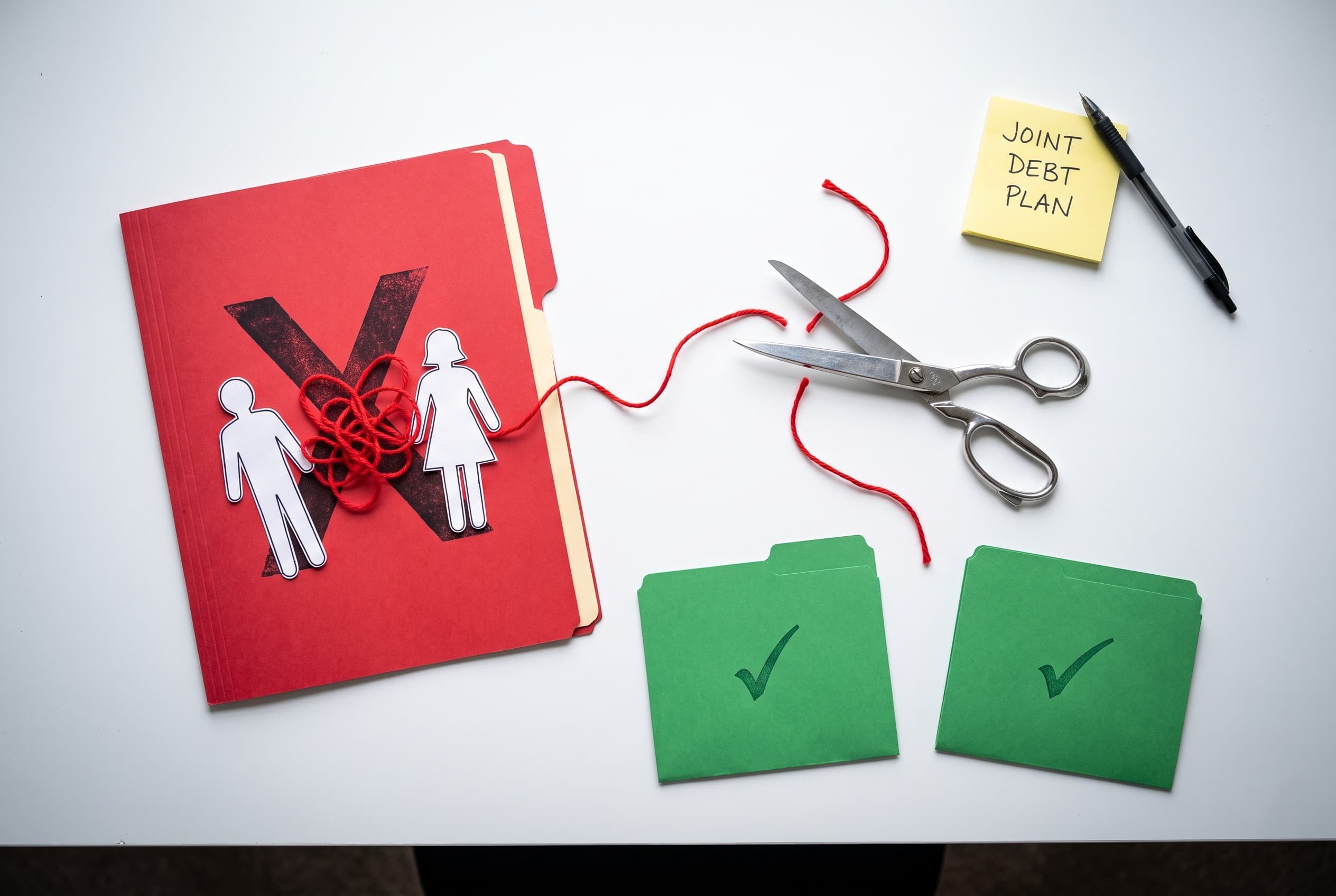 Top-down flat-lay photo on a clean white desk showing the concept of untangling joint debt. On the left, a red folder stamped