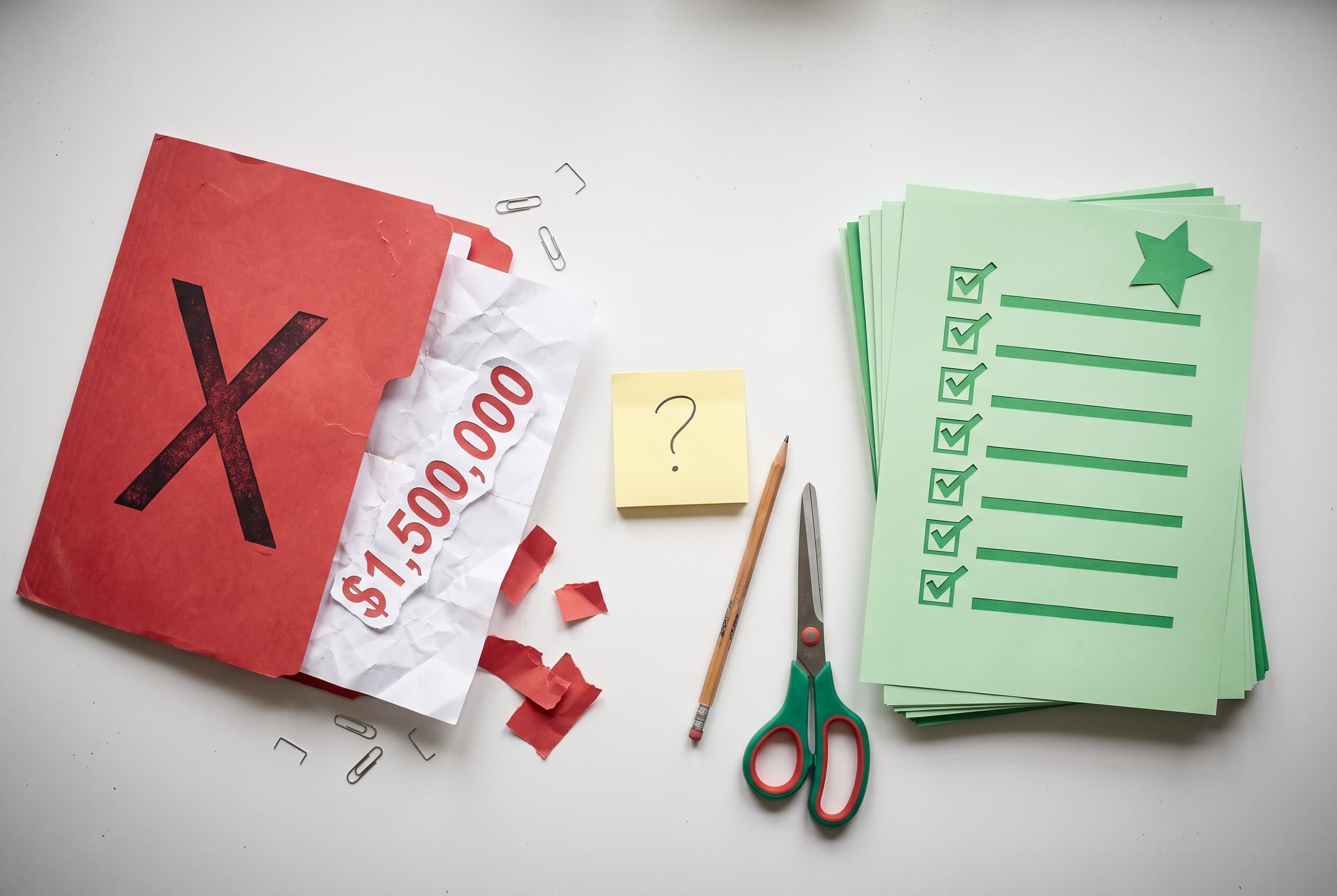 Top-down flat-lay photo on a clean white desk showing two distinct paper piles. On the left, a red folder stamped with a bold